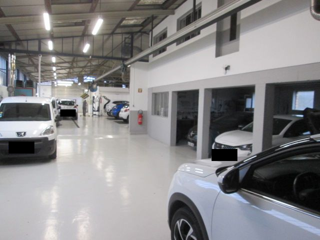 Intérieur d'un atelier de réparation automobile avec des voitures blanches, un sol lumineux et des baies de service.