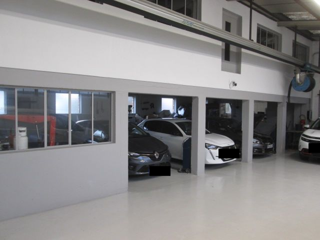 Un garage avec plusieurs places de stationnement pour voitures. Éclairage lumineux, couleurs gris et blanc.