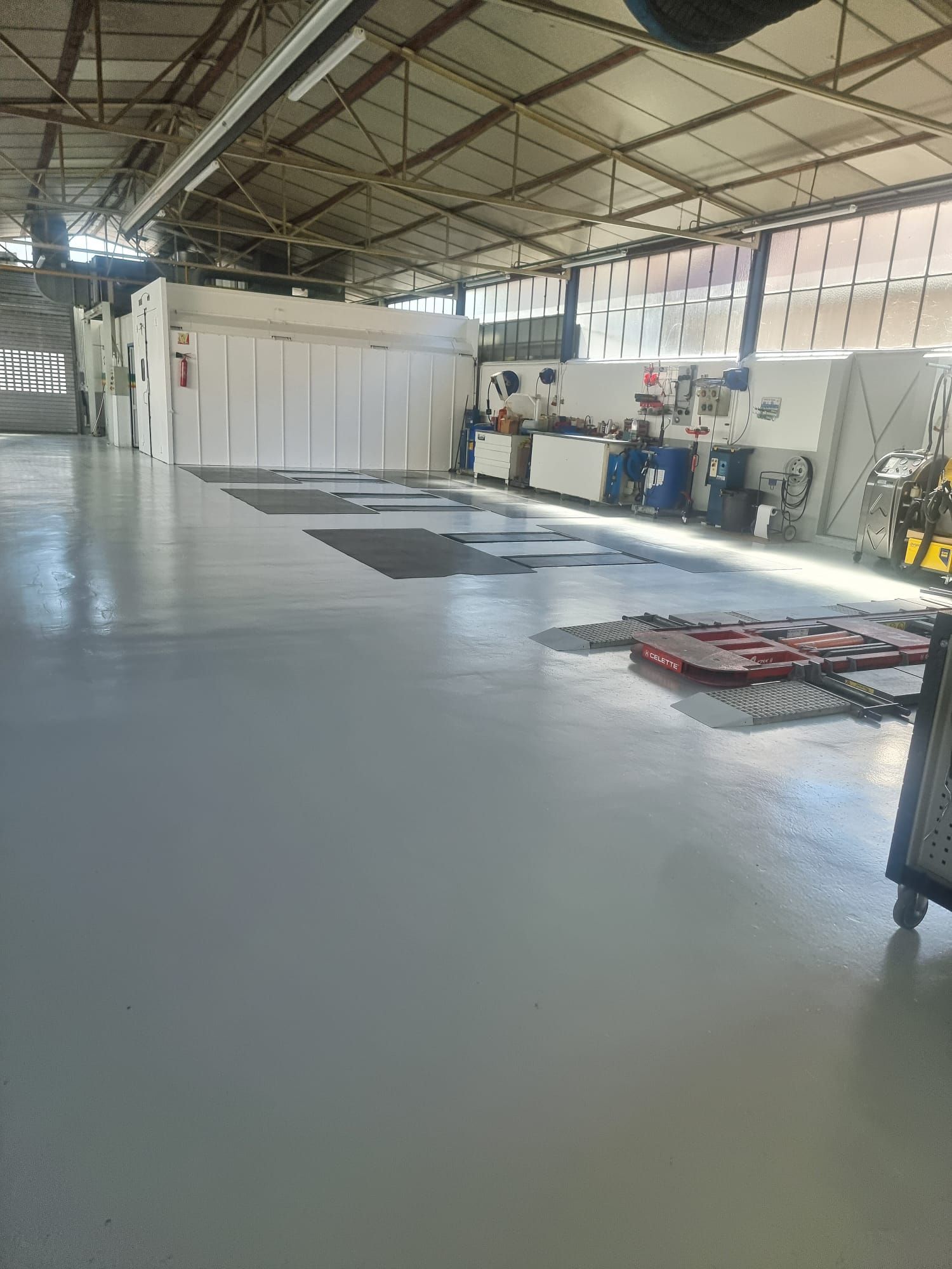 Un grand atelier automobile vide avec un sol gris clair, un plafond industriel et divers équipements.