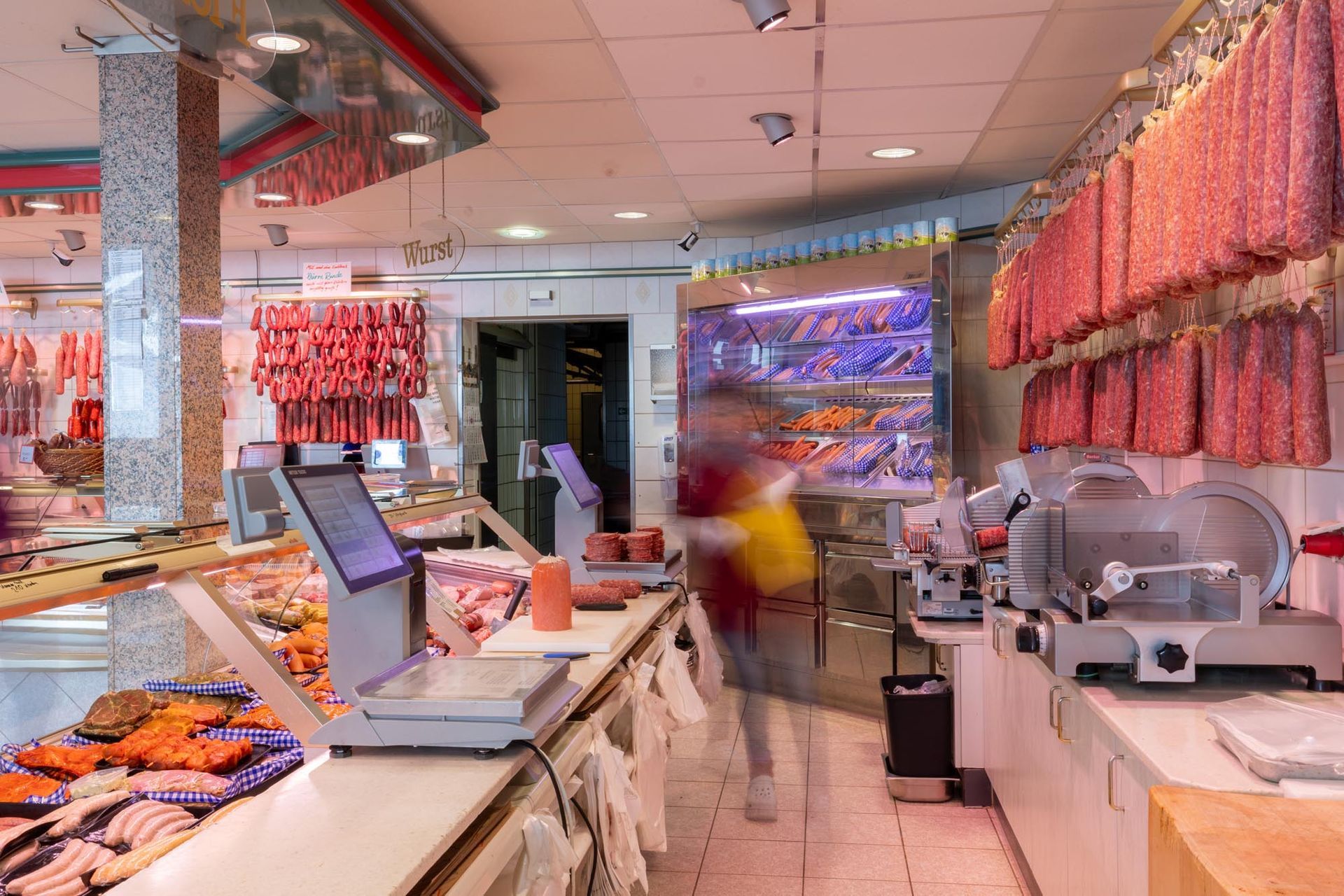 Die Theke einer Metzgerei mit hängenden Wurstwaren, Vitrinen und Schneidemaschinen in einem hellen Feinkostladen.