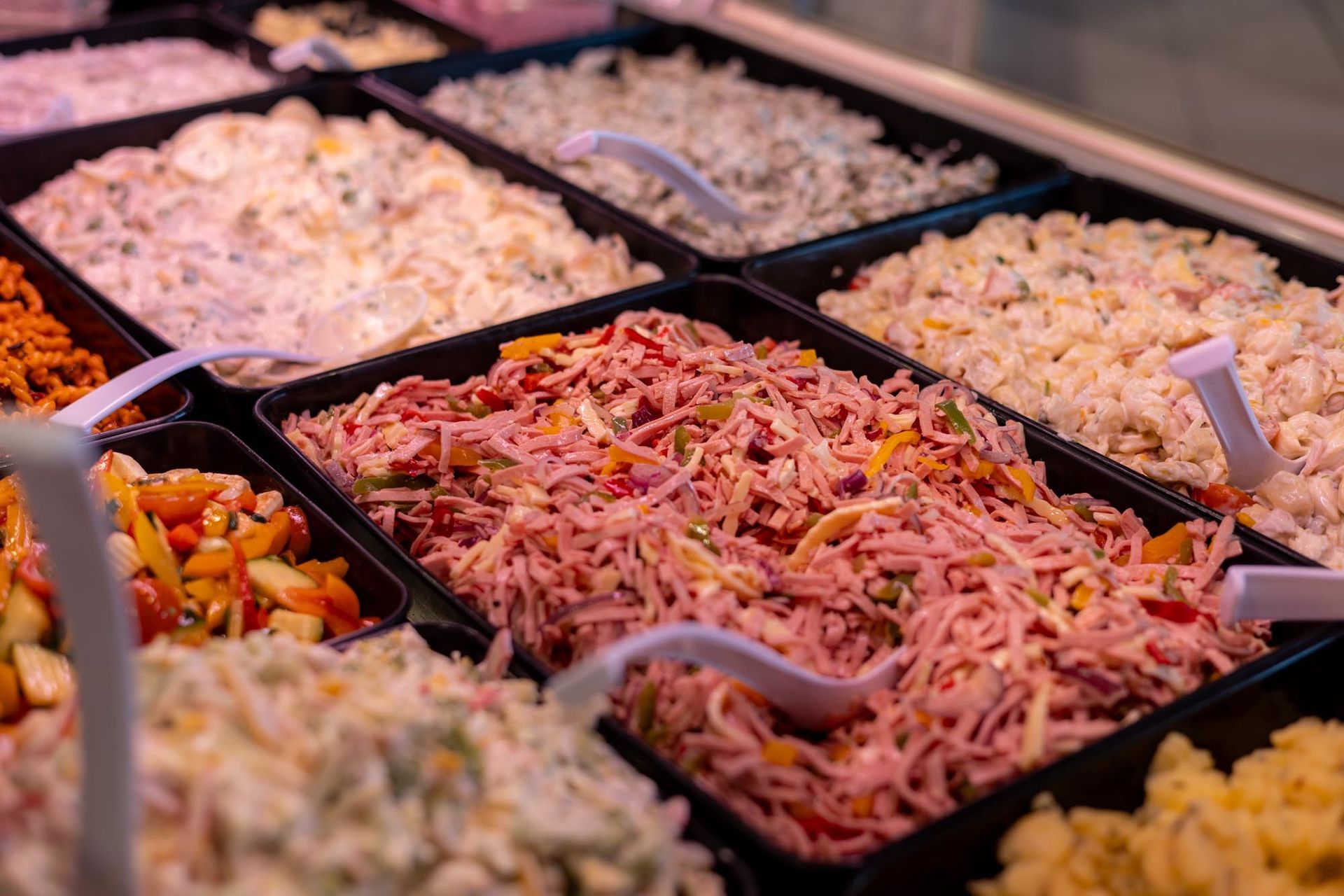 Buffetplatten mit verschiedenen Salaten und kalten Gerichten, in der Mitte rosa Nudelsalat.
