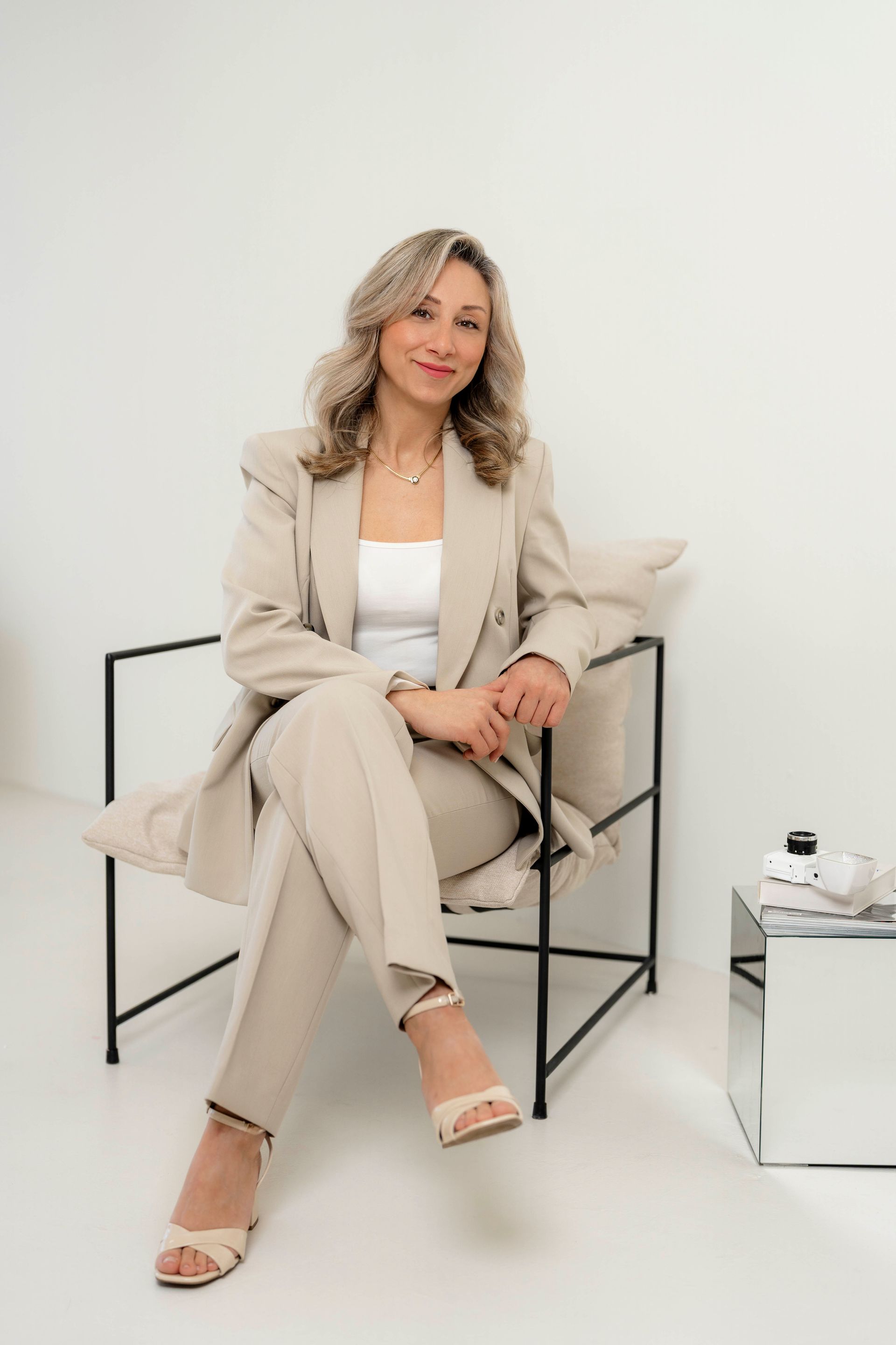 Eine Frau im Anzug sitzt auf einem Stuhl neben einem Spiegel.