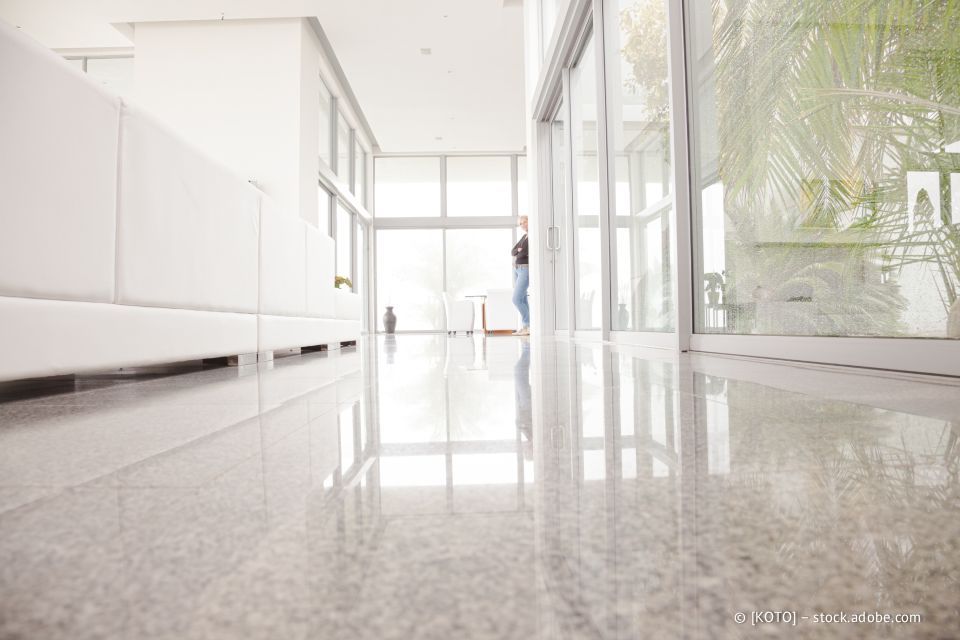 Heller, moderner Flur mit glänzendem Boden, weißen Wänden und großen Fenstern. Eine Person steht in der Nähe der Tür.