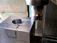 Una máquina está cortando un trozo cuadrado de metal con un agujero en él.