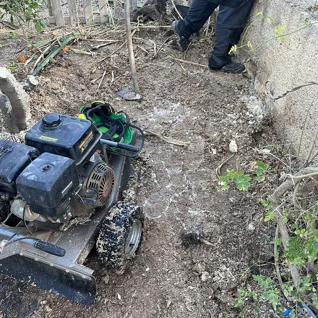 Una persona está parada junto a una trituradora de tocones en la tierra.