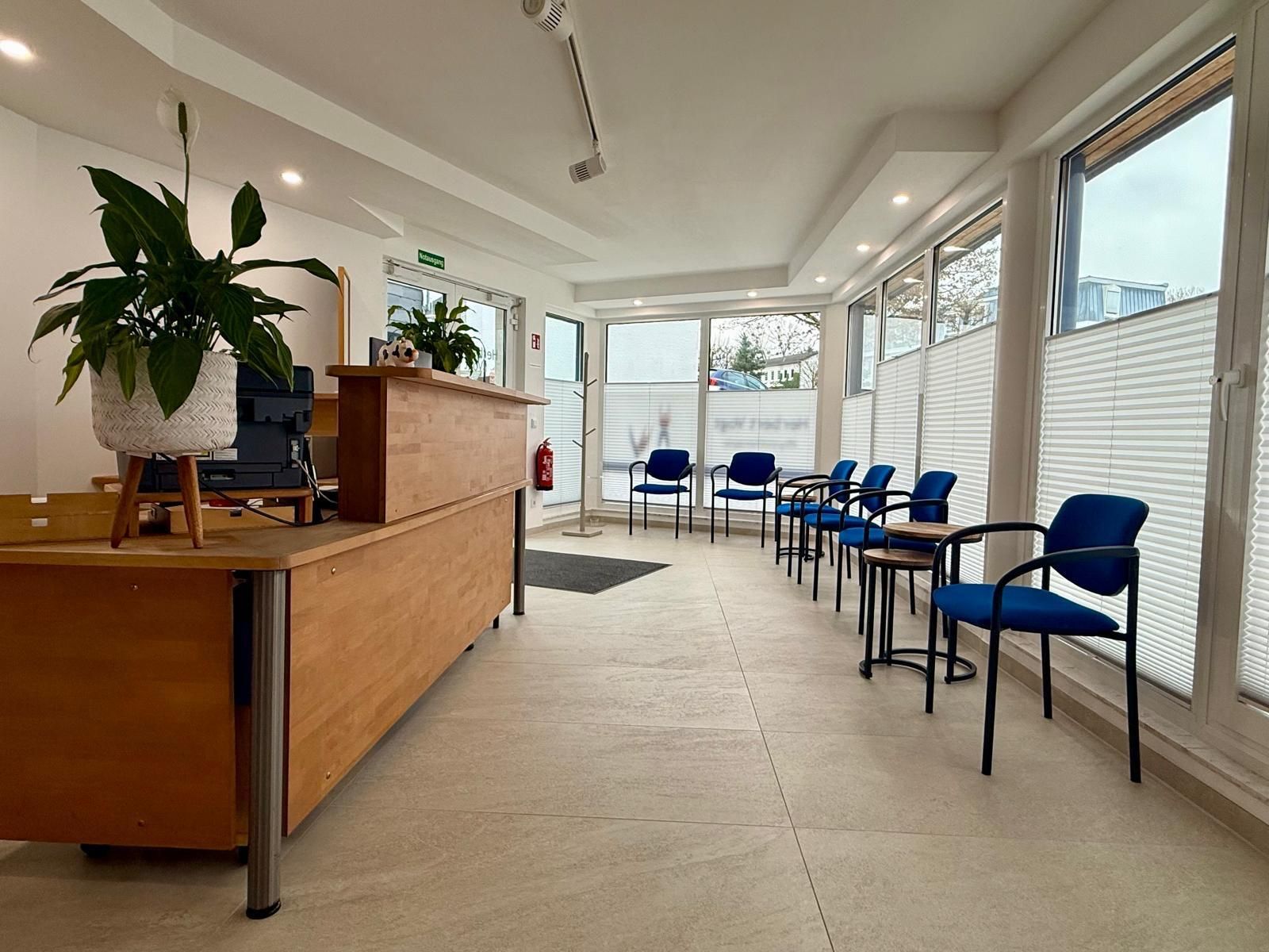 Ein Wartezimmer in einer Zahnarztpraxis mit Stühlen, Tischen und einem Fernseher.