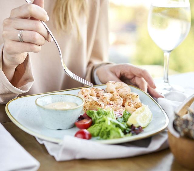 Una mujer está comiendo un plato de comida con un tenedor.