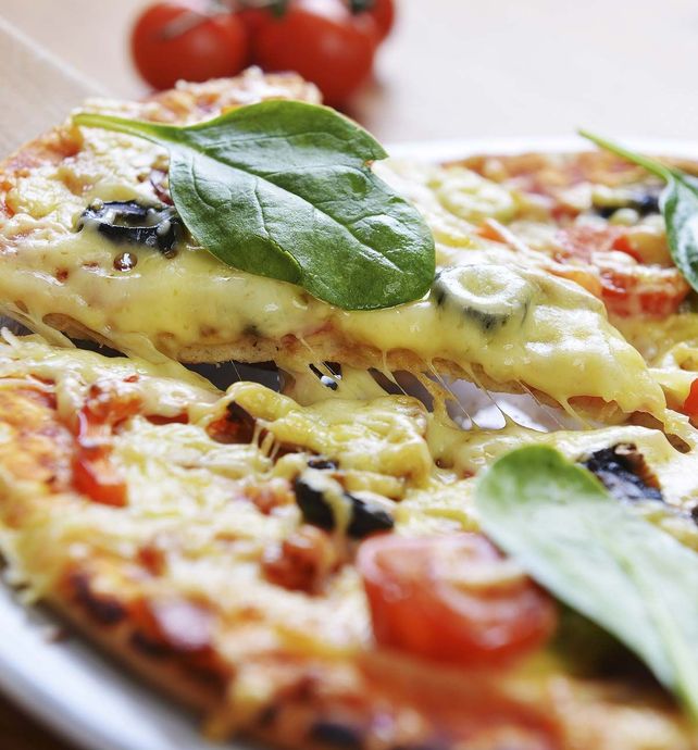 Una pizza con espinacas, aceitunas y tomates en un plato.
