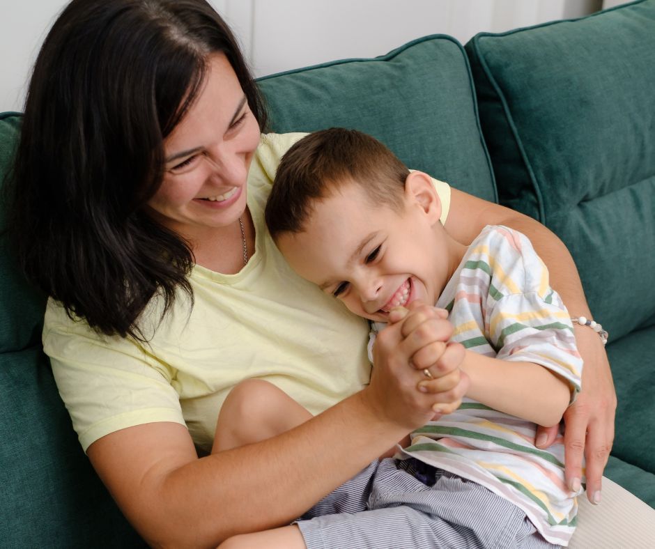 Woman and child laughing together on a green couch. Woman is holding the child and tickling.