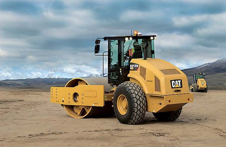 Un rodillo compactador de gato amarillo está sentado encima de un campo de tierra.