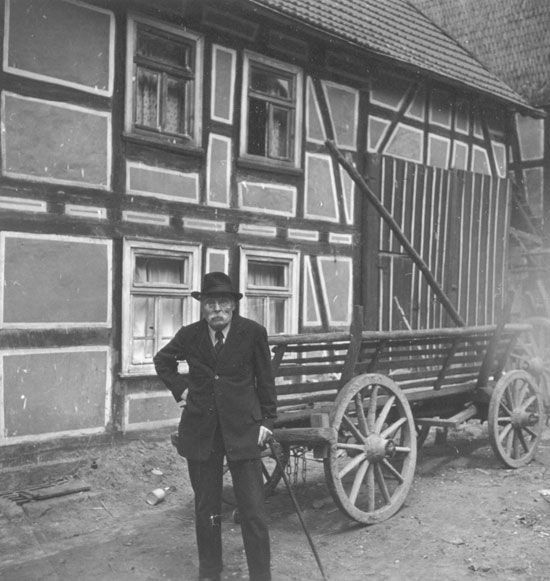 Schwarz-Weiß-Bild, ein Herr steht mit einem Karren vor einem Haus