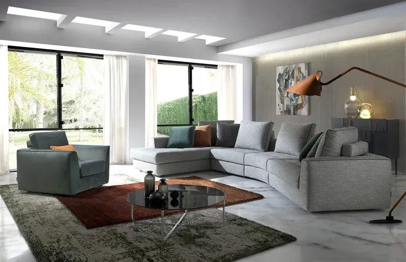 Un salón moderno y minimalista con un sofá modular gris, un sillón a juego y una mesa de centro circular de cristal.