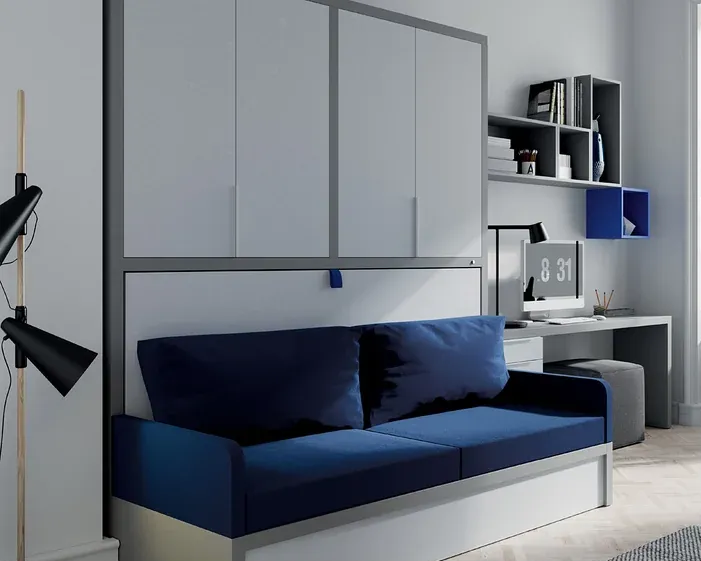 Un sofá azul marino colocado frente a una cama Murphy blanca, con un escritorio