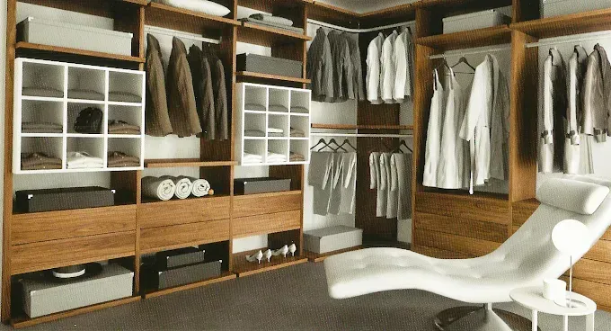 Un vestidor amplio y moderno con estantes de madera, perchero, organizadores blancos y un sillón blanco.