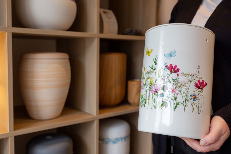 Auf einem Tisch steht eine kleine weiße Urne neben einem Strauß weißer Blumen.