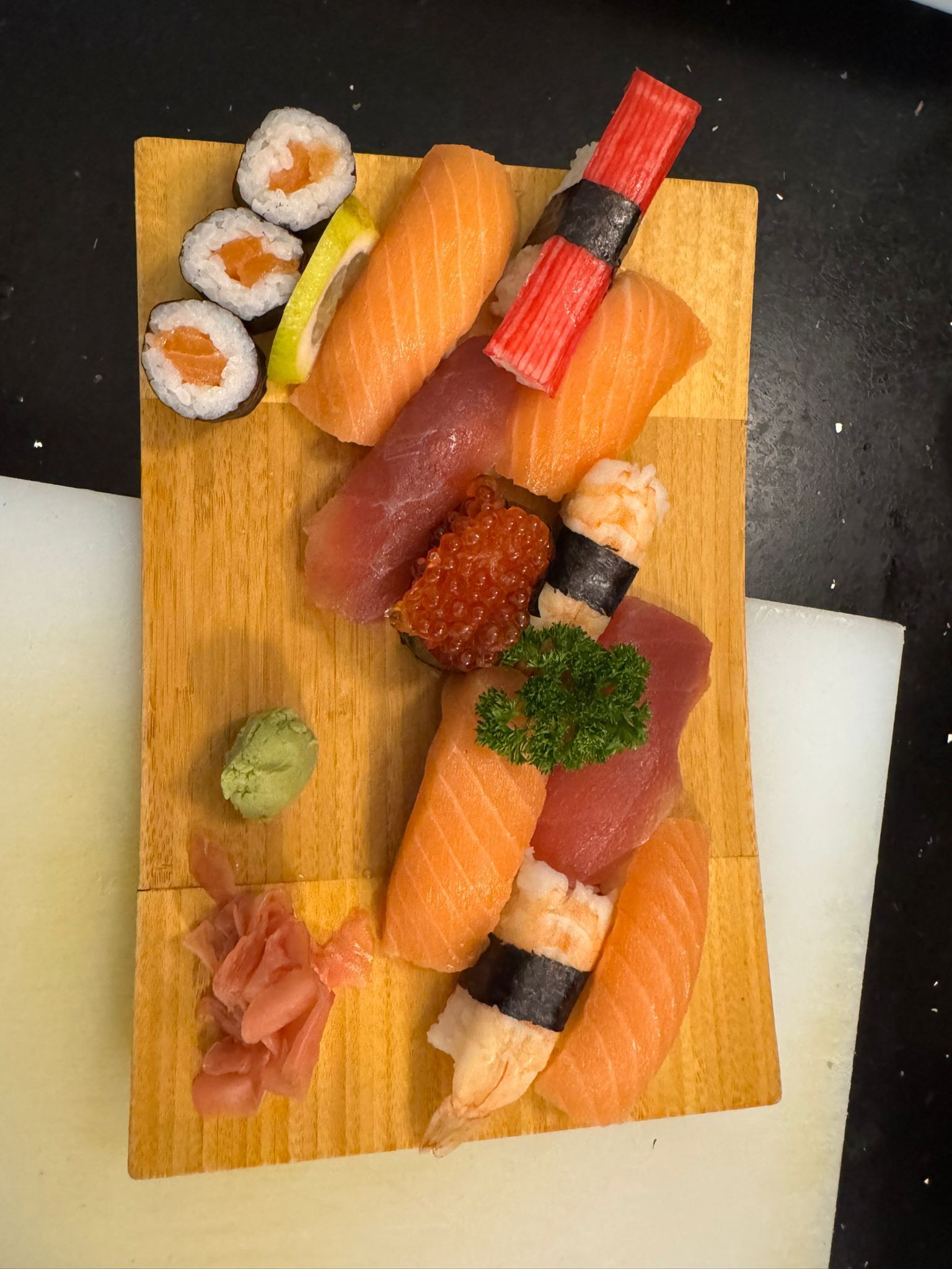 Sushi-Platte auf Holzbrett, bestehend aus Lachs, Thunfisch, Garnelen-Nigiri, Rollen und Ingwer.