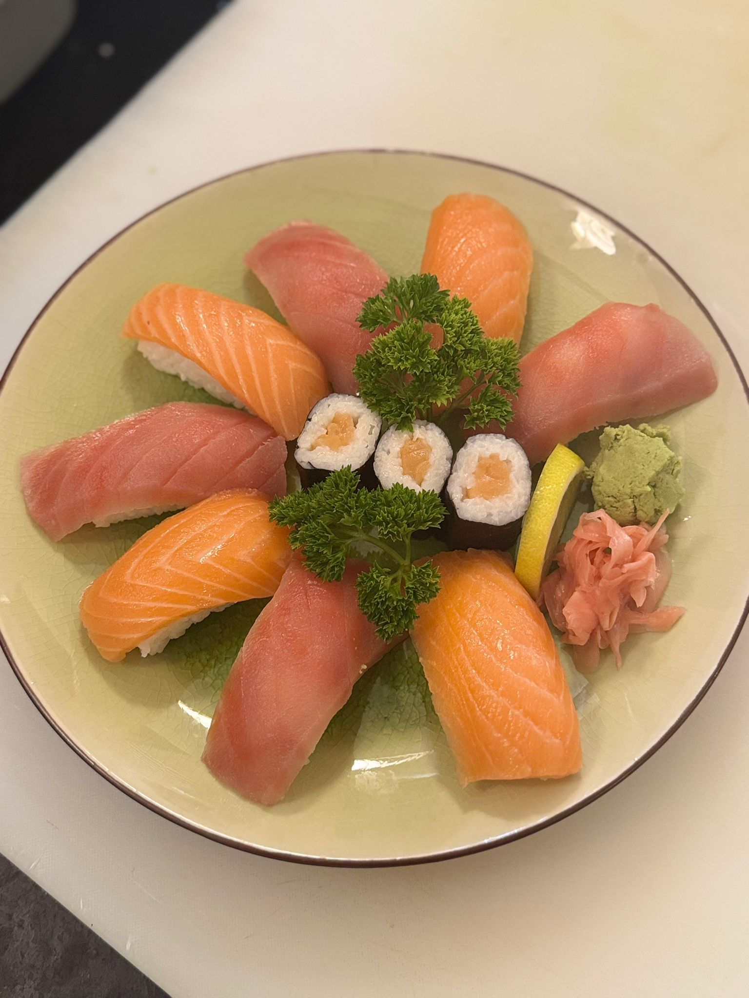 Sushi-Platte mit Lachs, Thunfisch-Nigiri und Maki-Rollen, garniert mit Wasabi, Ingwer und Petersilie auf einem grünen Teller.