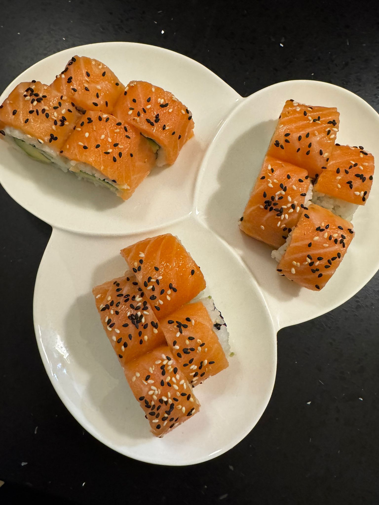 Sushi-Rollen mit orangefarbenem Lachs und schwarzen Sesamsamen auf weißen Tellern.