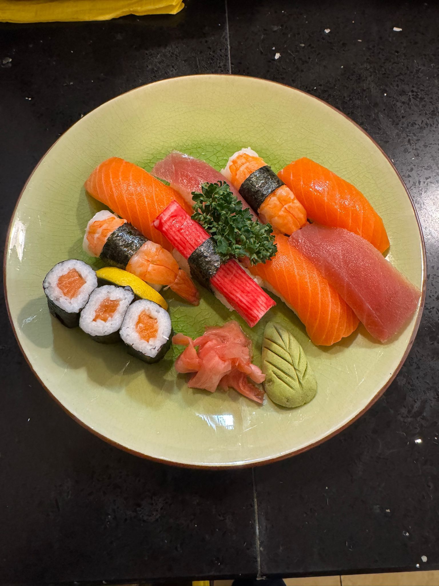 Sushi-Platte auf grünem Teller: Lachs, Thunfisch, Krabbenfleisch, Nigiri, Maki-Rollen, Ingwer, Wasabi.