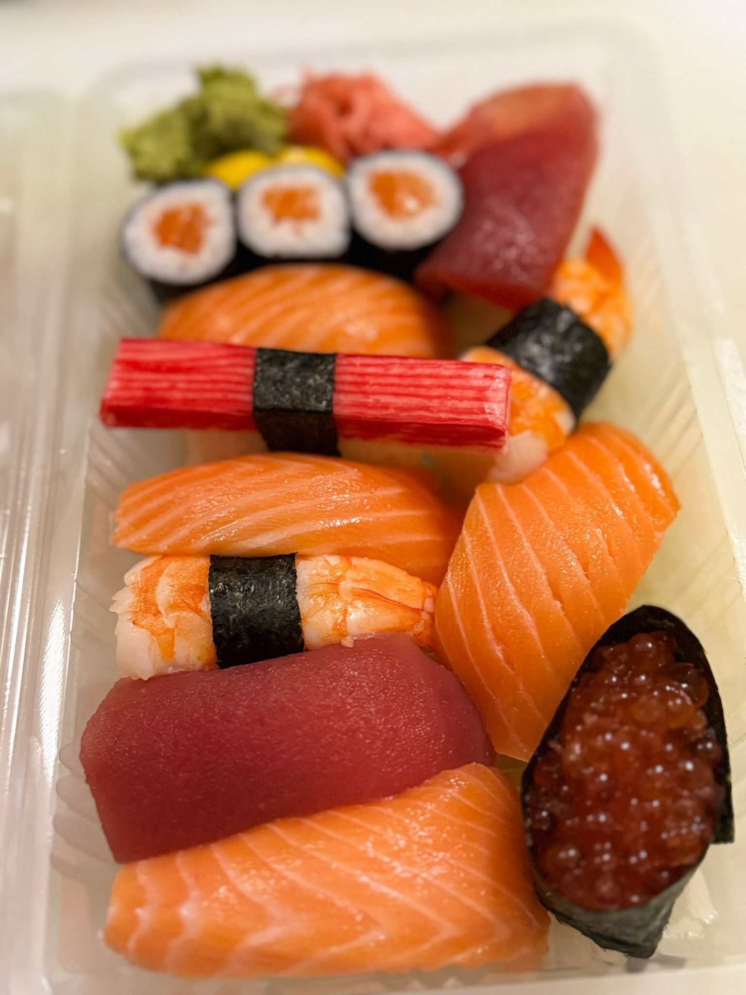 Sushi-Sortiment in einem durchsichtigen Plastikbehälter: Lachs, Thunfisch, Garnelen, Krabben, Rogen und Maki-Rollen.