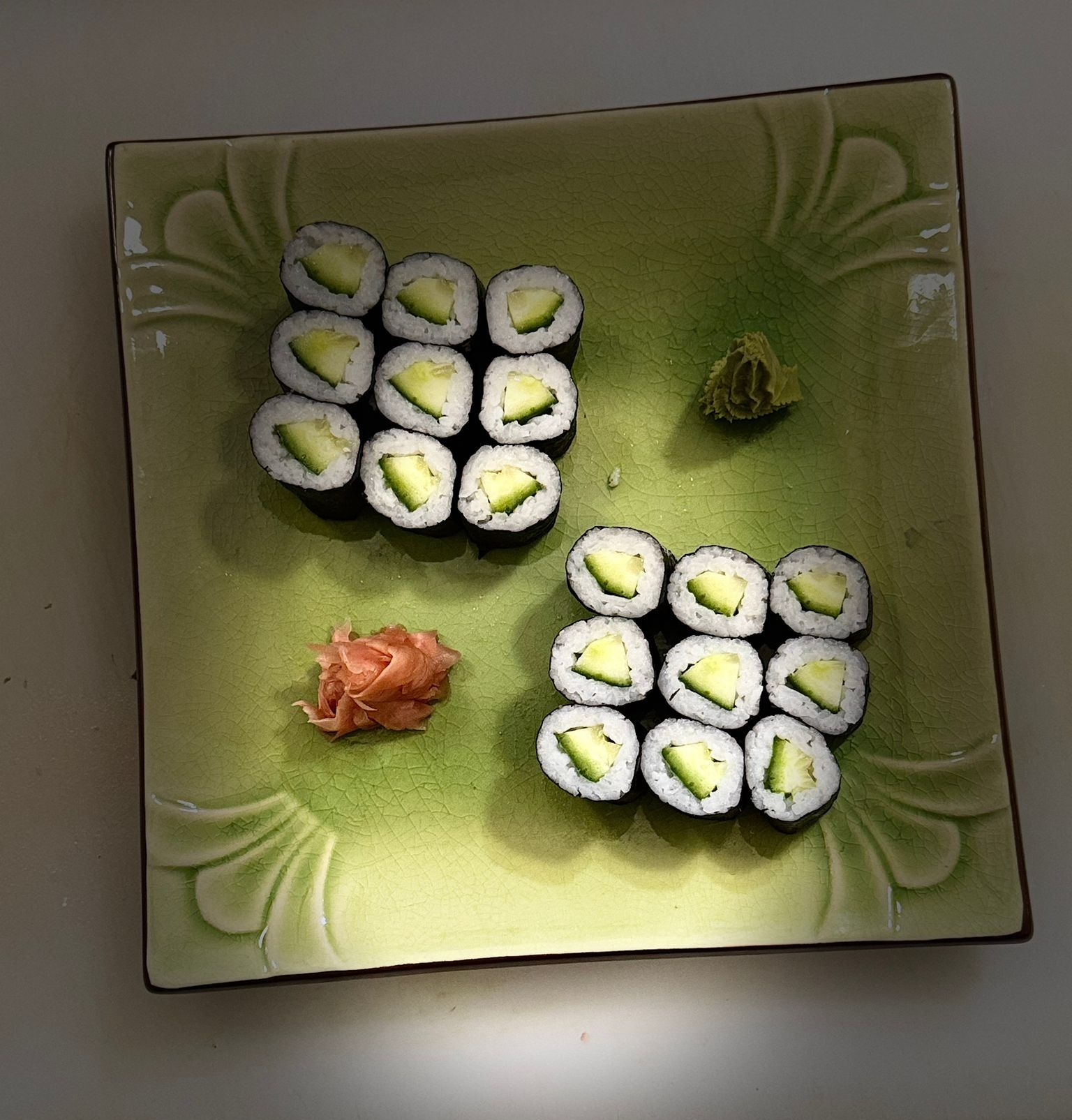 Sushi-Rollen mit Gurkenfüllung, Wasabi und eingelegtem Ingwer auf einem grünen Teller.