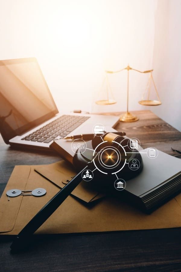 Ordenador portátil, mazo, balanza de la justicia sobre un escritorio de madera con documentos.