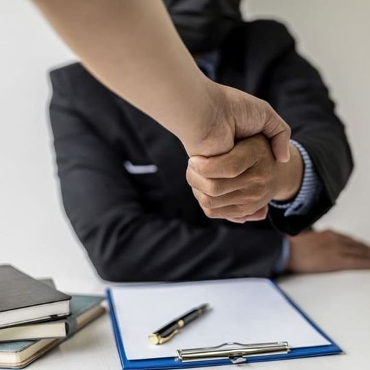 Un apretón de manos sobre un contrato sobre un escritorio, en un entorno empresarial.
