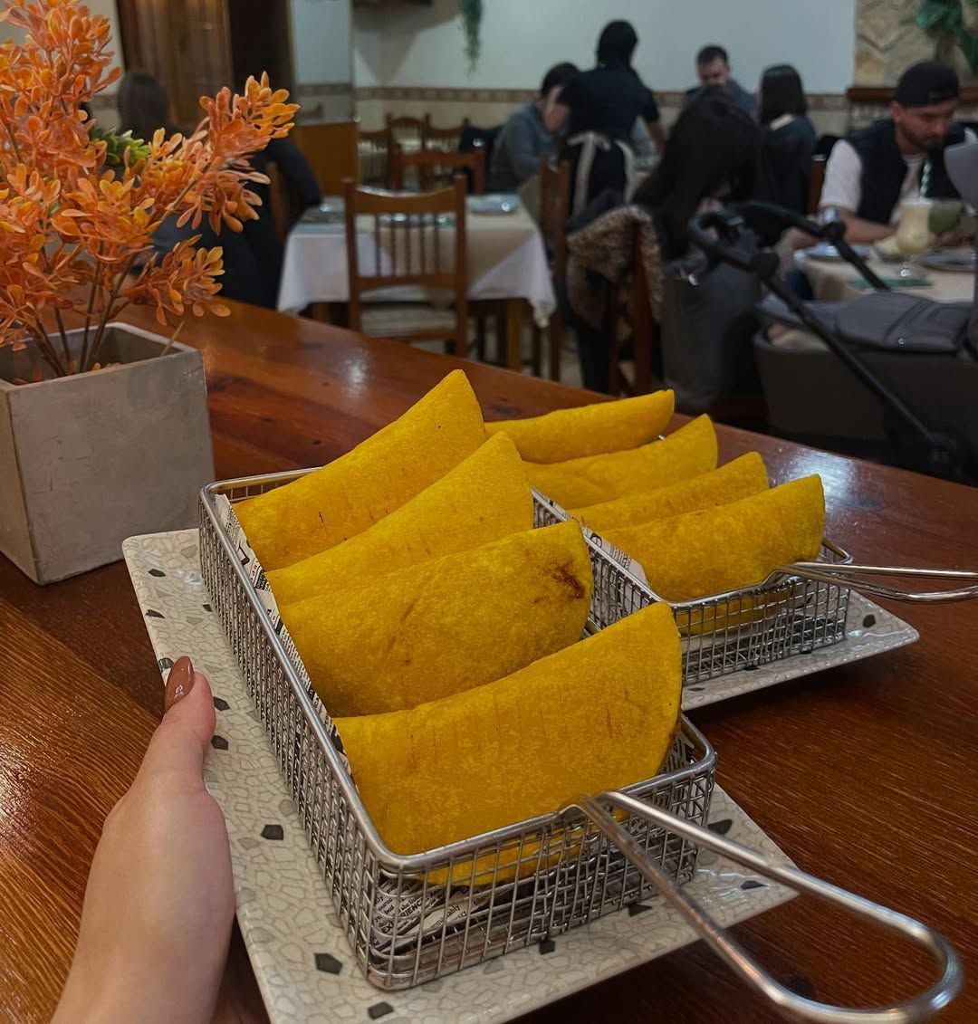Una mano sosteniendo una canasta de empanadas de maíz sobre una mesa en un restaurante.