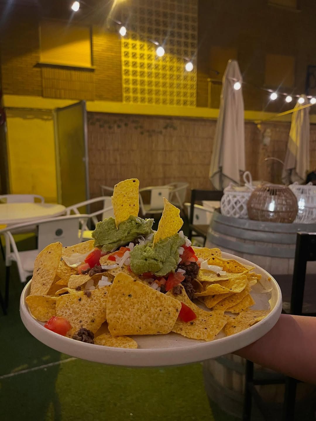 Un plato de nachos con guacamole y aderezos, sostenido en el restaurante.