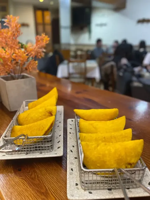 Dos bandejas de empanadas de color amarillo dorado sobre una mesa de madera, interior de restaurante con fondo borroso.