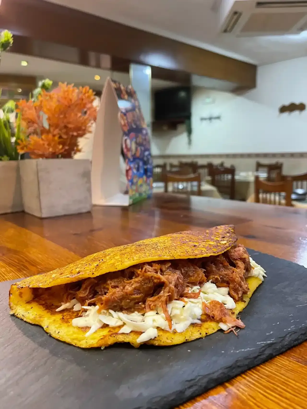 Arepa rellena de carne desmenuzada y queso sobre una tabla negra. Mesa de madera.