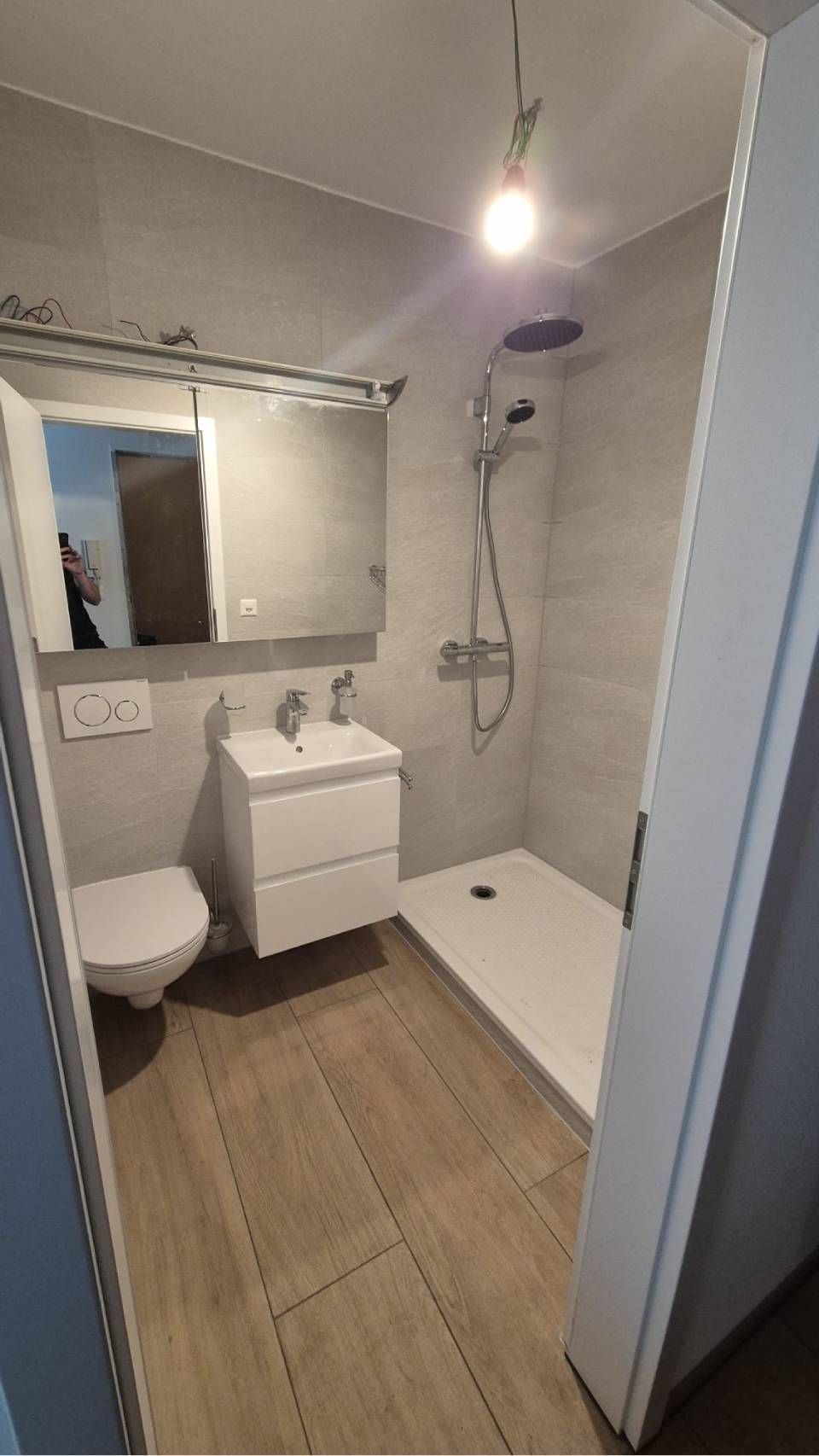 Ein modernes Badezimmer mit ebenerdiger Dusche mit Glasabtrennung, weissem Waschtisch, wandhängender Toilette und Holzfliesen.