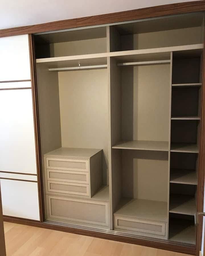 Armario abierto con estantes de madera, espacio para colgar ropa, cajones y puertas correderas a la izquierda.