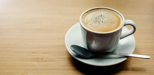 Taza de café sobre un platillo con una cuchara sobre una mesa de madera, con espuma encima.