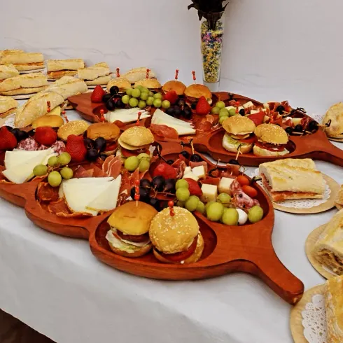Variedad de aperitivos y sándwiches dispuestos en tablas de madera en una mesa tipo bufé.