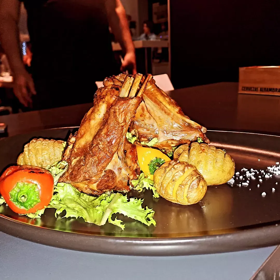 Costillas a la parrilla servidas en un plato con maíz asado, verduras y hierbas en un ambiente de restaurante 