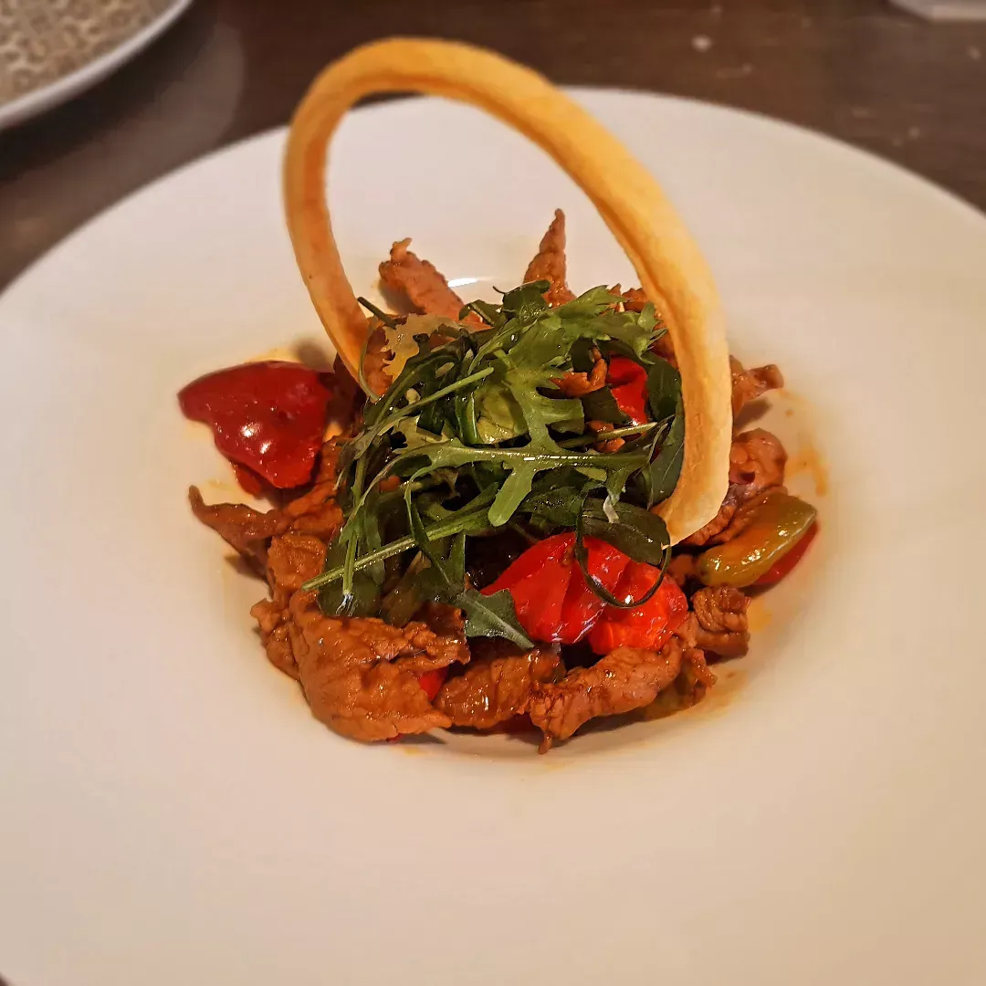 Aperitivo gourmet con tomates rojos, verduras y un crujiente aro de pan en un plato blanco.