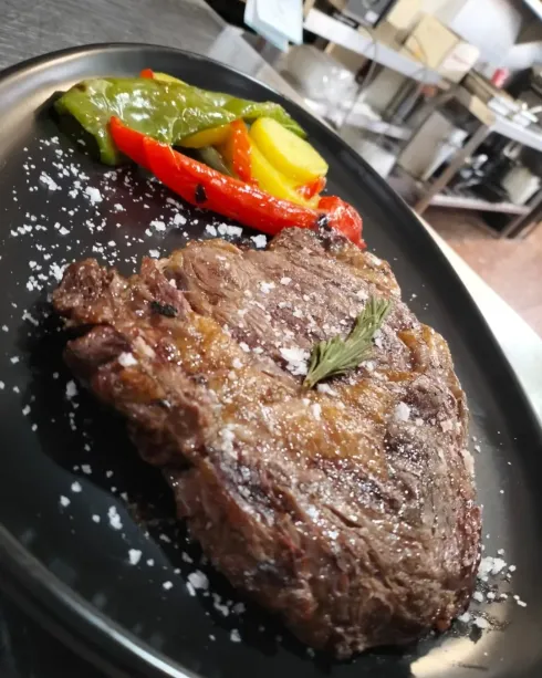 Filete a la parrilla en un plato negro con sal y pimientos rojos, verdes y amarillos asados.