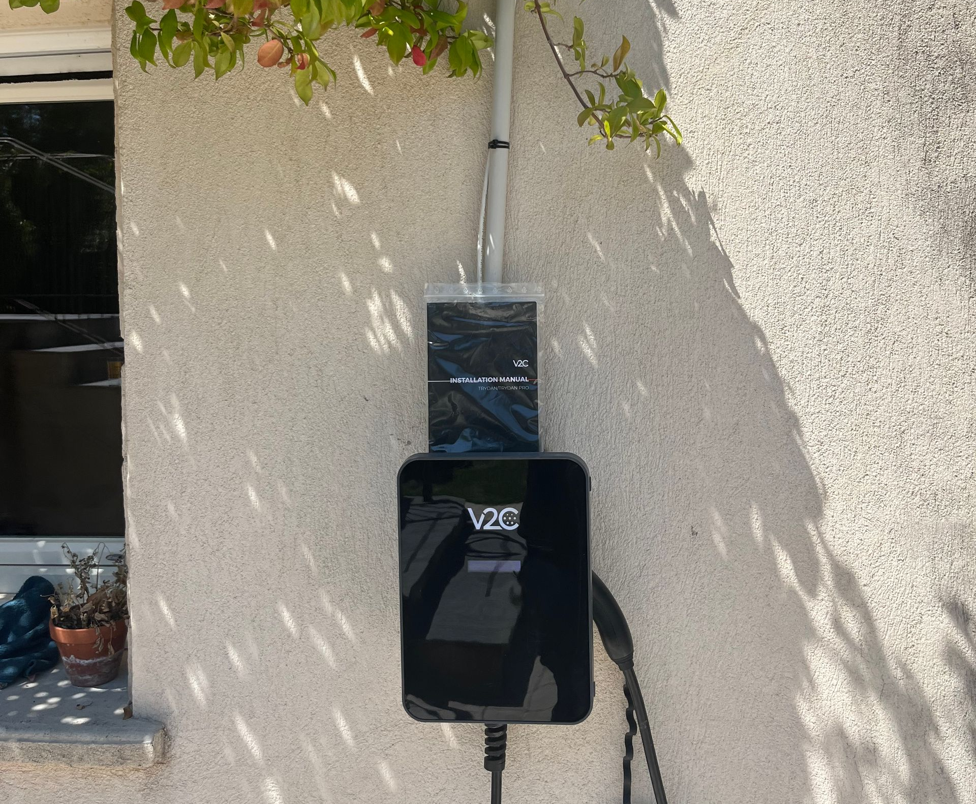 Chargeur EV V2E noir monté sur un mur en stuc beige avec câble suspendu.