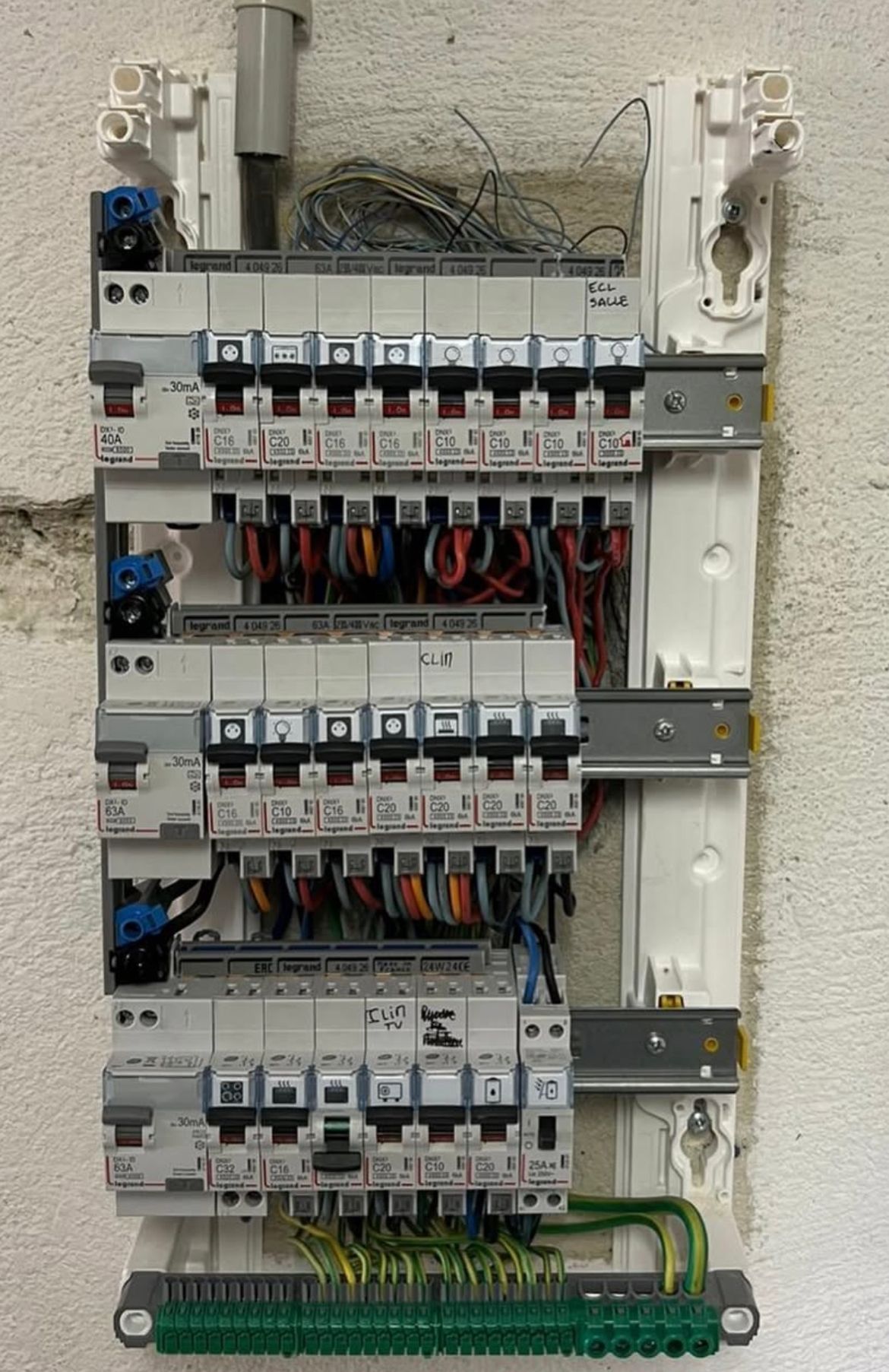 Panneau électrique avec plusieurs disjoncteurs, fils et une barre de terre, monté sur un mur.