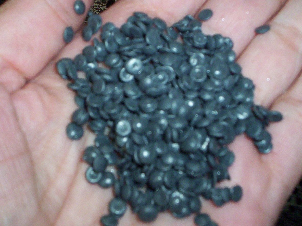 La palma de una persona sosteniendo un montón de pequeñas bolitas de resina plástica de color gris oscuro.