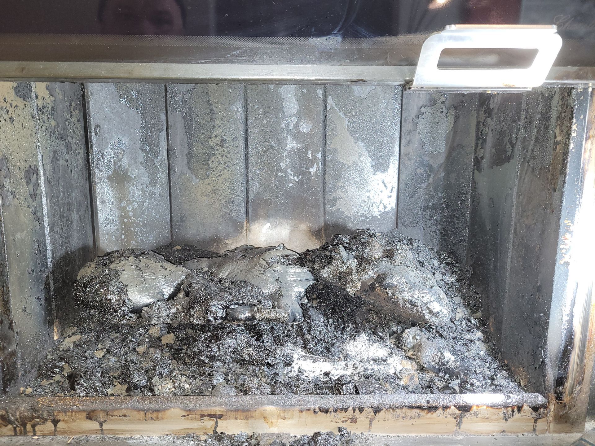 Intérieur de la cheminée avec cendres et suie. Des débris gris et noirs recouvrent la base.