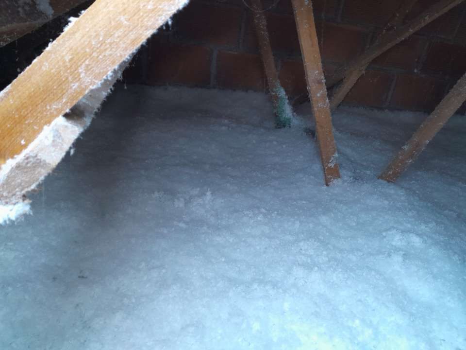 Isolation en cellulose dans un grenier entre des chevrons en bois et contre un mur en briques.