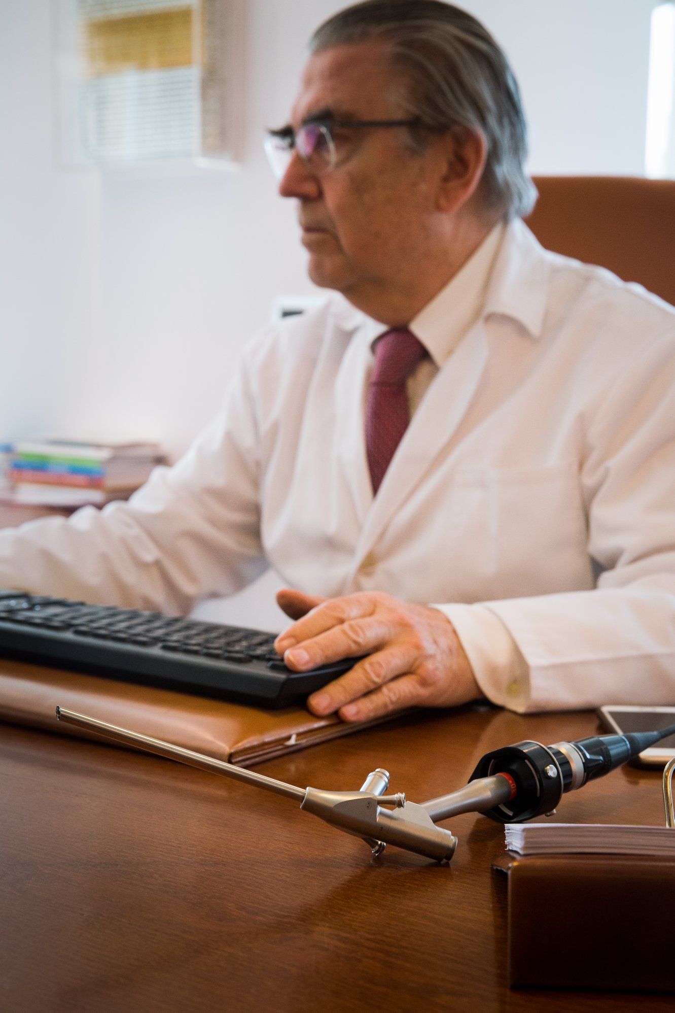 Un hombre con bata de laboratorio y corbata está sentado en un escritorio utilizando una computadora.