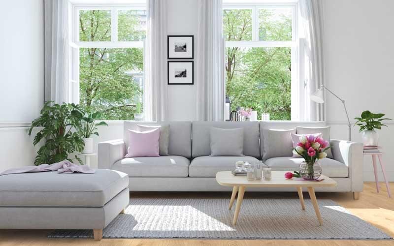 Ein Wohnzimmer mit Couch, Couchtisch, Ottomane und zwei Fenstern.