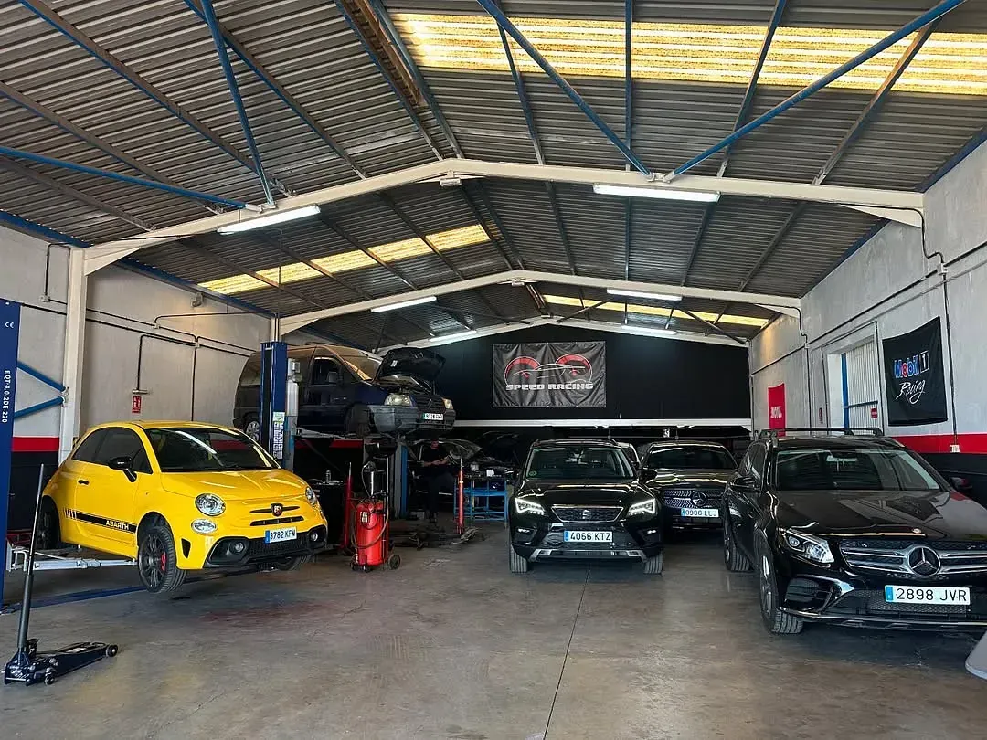 Un coche amarillo está aparcado en un garaje al lado de un coche negro.