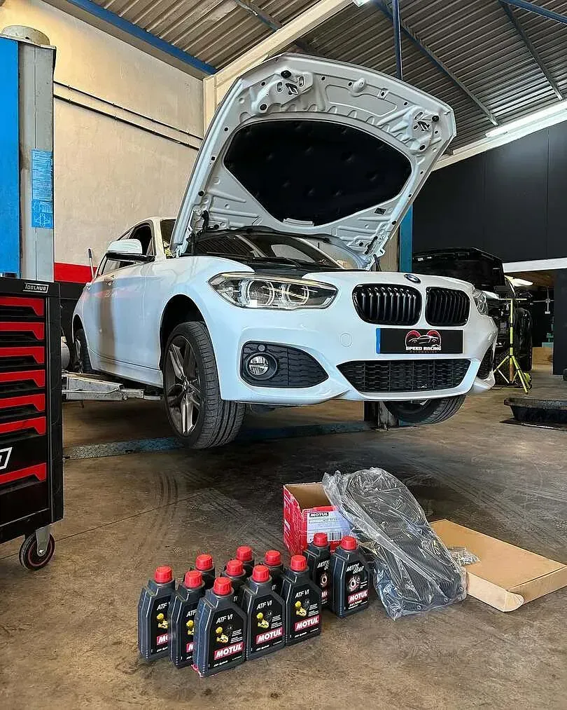 Un BMW blanco está aparcado en un garaje con el capó levantado.
