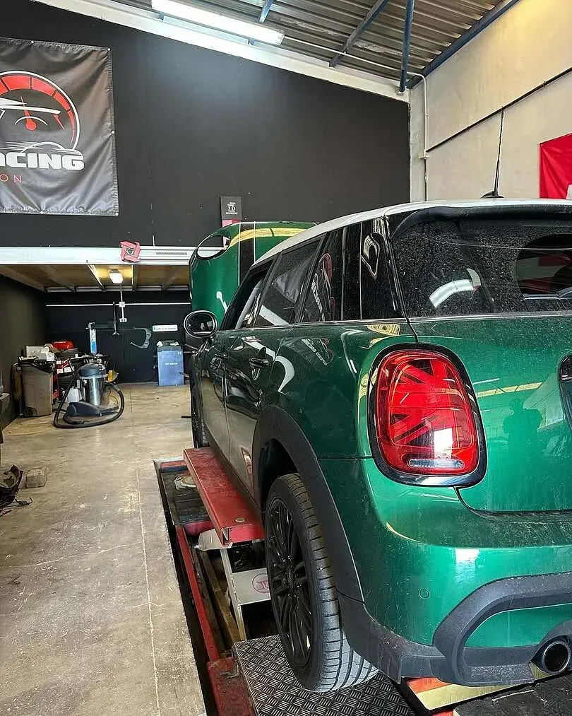 Un Mini Cooper verde está sentado en un elevador en un garaje.
