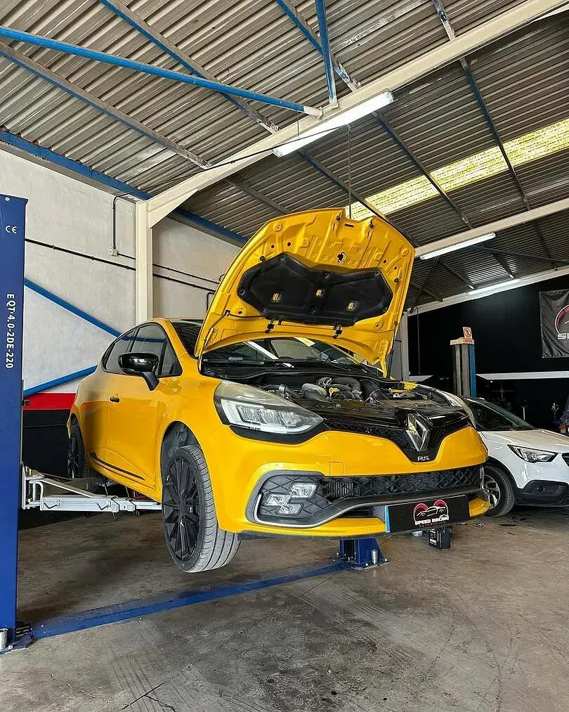 Un coche amarillo con la capota levantada está en un elevador en un garaje.