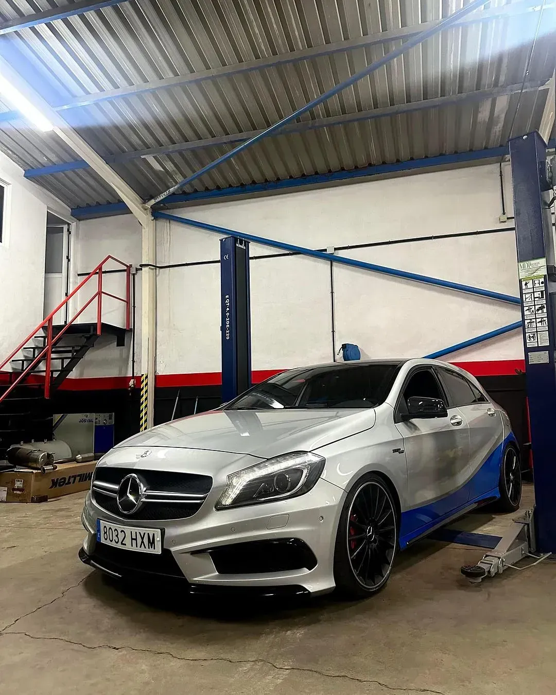 Un Mercedes Benz Clase A plateado está aparcado en un garaje sobre un elevador.